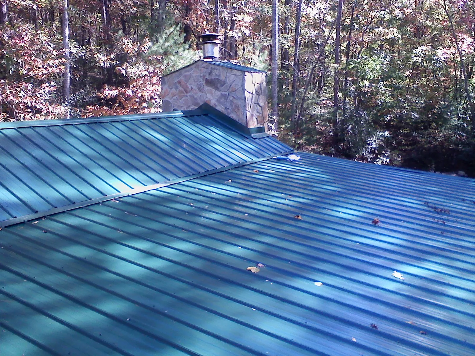 New green metal roof and stone chimney surrounded by autumn woods in Hollis
